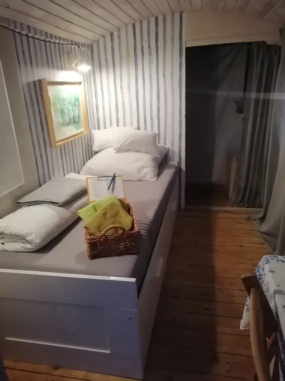 Bett im Bauwagen vor heller Riffelwand, Bild und Leselampe