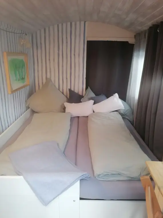Bett mit Kissen und Decke, davor ein Vorhang