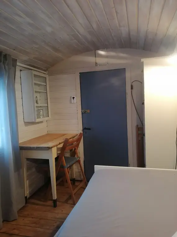 Tisch mit Stuhl am Fenster, daneben die Tür des Bauwagens