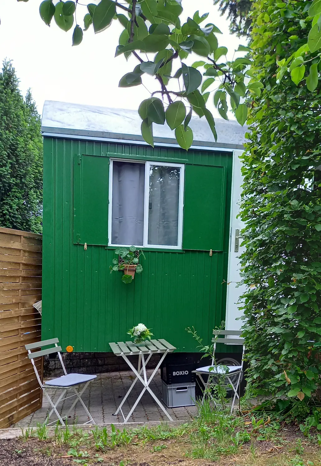 Grüner Bauwagen mit Terrasse, Bistrotisch und Stühlen im Garten