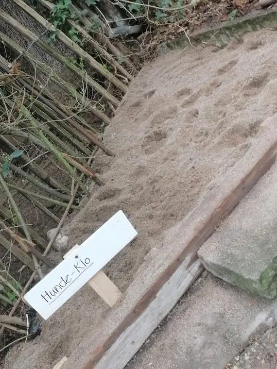 Handgeschriebenes Schild „Hunde-Klo" an einer Sandfläche