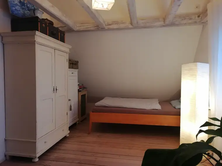 Bett und großer weißer Schrank im Zimmer mit sichtbaren Deckenbalken
