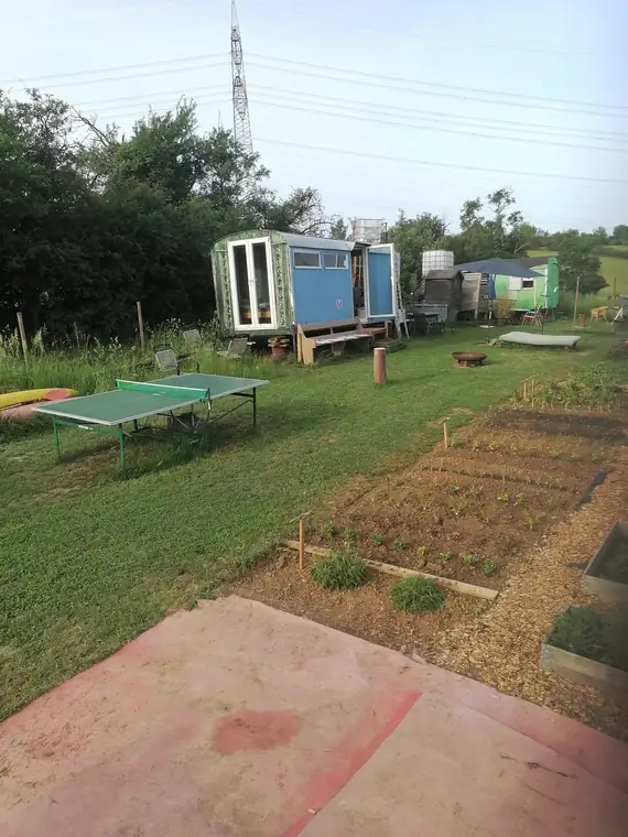 Blick von der Terrasse über Tischtennisplatte und frisch angelegte Beete zum Bauwagen