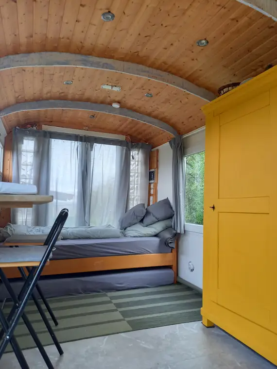 Bett unter dem Fenster, Holzdecke, daneben eine gelbe Tür
