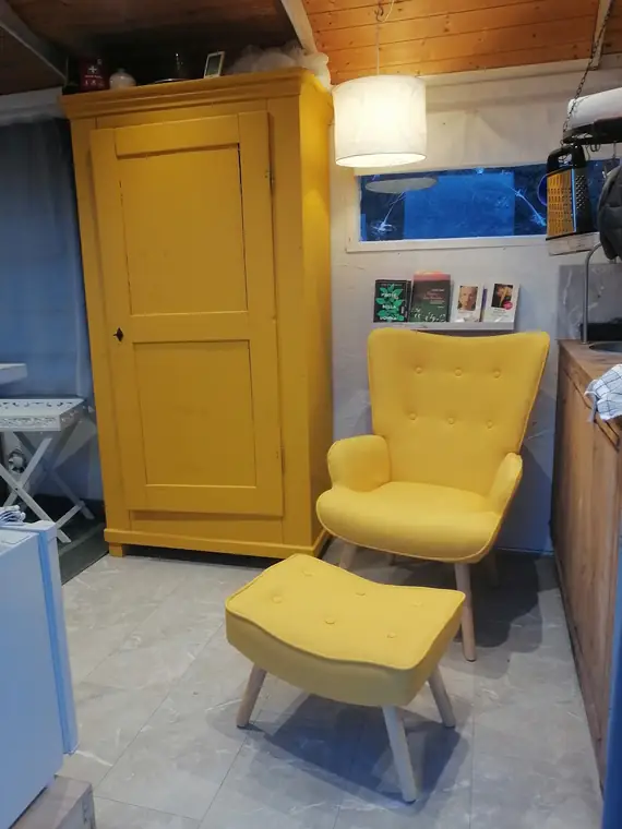 Gelber Schrank und gelber Sessel mit Hocker unter einer Lampe