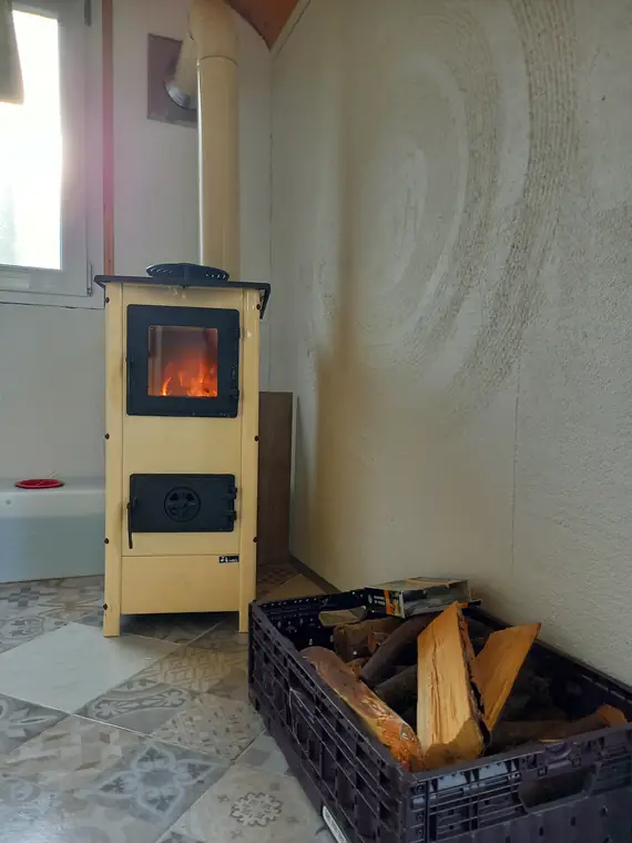 Cremefarbener Holzofen mit Feuer, daneben eine Kiste Brennholz