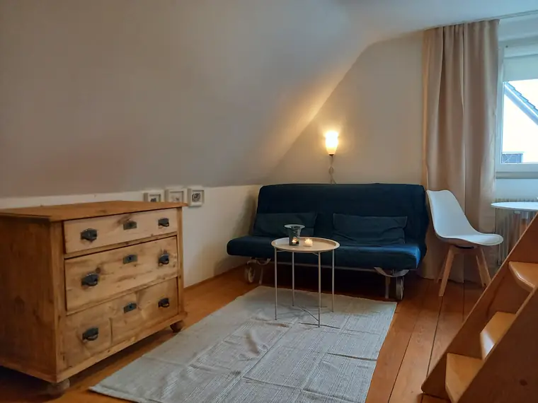 Alte Holzkommode, blaue Schlafcouch und runder Beistelltisch auf Dielenboden
