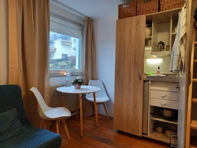 Geöffneter Schrank mit Kochnische, daneben Esstisch und Couch